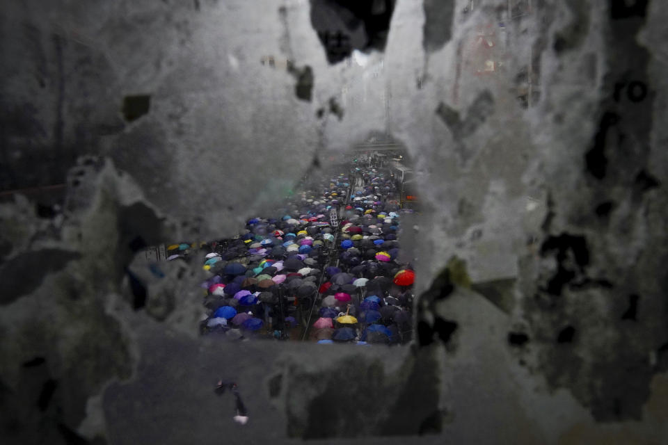 Protesters carrying umbrellas are seen through the tainted glass panel on the pedestrian overhead bridge as they march on a street in Hong Kong, Sunday, Oct. 6, 2019. Thousands of protesters braved the rain to march in central Hong Kong as a second legal attempt to block a mask ban at rallies to quash four months of pro-democracy demonstrations was rejected by the court. (AP Photo/Vincent Yu)