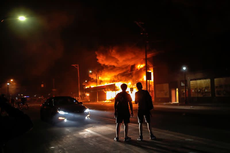 People look on from a distance after protesters set fire to a liquor store as demonstrations continue in Minneapolis