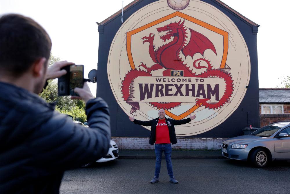 A Wrexham fan poses for a picture by the Welcome to Wrexham mural which was painted to publicise the documentary.