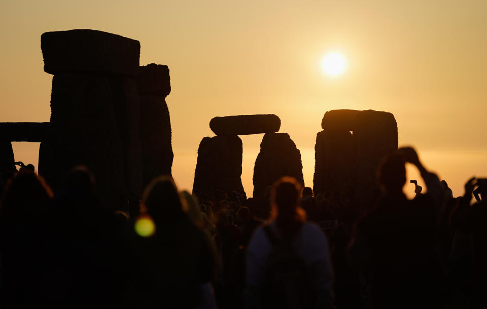 The sun rises behind the stone circle as people gather to take part in the Summer Solstice at Stonehenge in Wiltshire