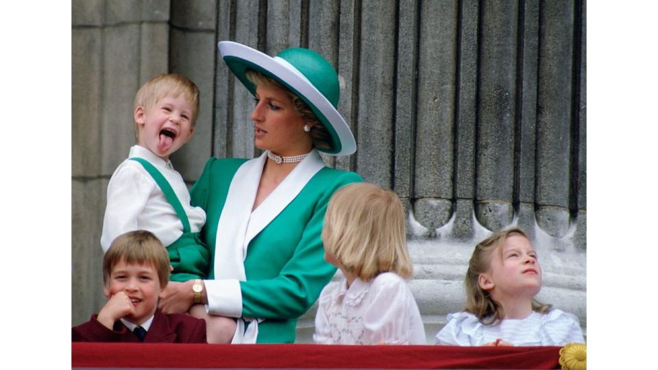 Princess Diana holding a young Prince Harry who is sticking out his tongue