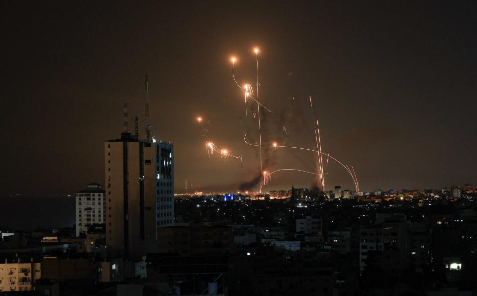 An image shows the flight path of missiles from the Iron Dome, diverting to hit mortar and missile shots coming in from Gaza, over a town at night. Some rockets are shown to have exploded as evidenced by bright debris raining down. 