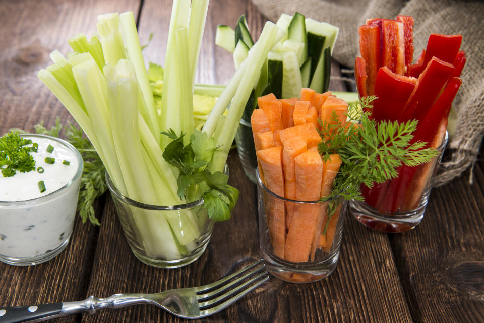 A variety of fresh, raw vegetables including celery, carrots, cucumber and peppers, cut into sticks and placed in glass cups