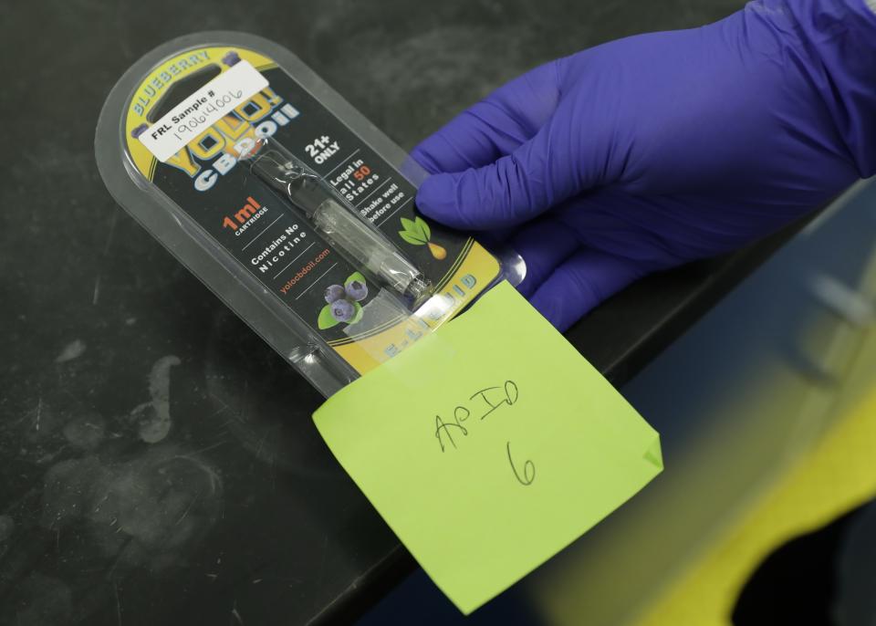 A researcher holds a Yolo! brand CBD vape oil cartridge and its packaging at Flora Research Laboratories in Grants Pass, Ore., on July 17, 2019. Authorities blamed Yolo for sending people to emergency rooms in Utah, saying it contained a dangerous synthetic marijuana. The cartridge pictured here was provided to The Associated Press by a South Carolina man who says he nearly died after puffing it. Testing commissioned by AP shows it contained the same synthetic marijuana that caused the illnesses in Utah. (AP Photo/Ted Warren)