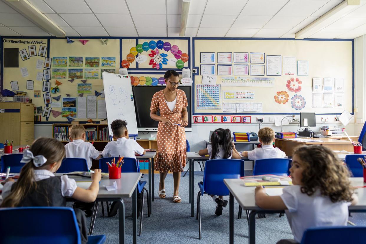 Primary school students sitting in a classroom being taught by a teacher in the North East of England. The pupils are learning on mini whiteboards.