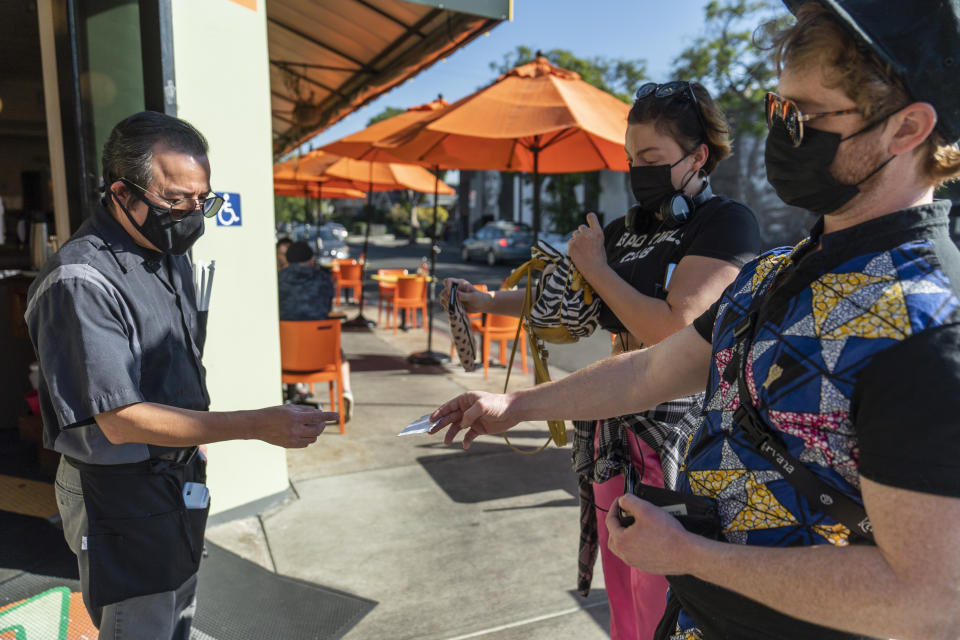 Waiter Juan Rodrigues, left, asks patrons to show their vaccination cards before entering the Fred 62 restaurant in the Los Feliz neighborhood of Los Angeles, Monday, Nov. 29, 2021. Enforcement began Monday in Los Angeles for one of the strictest vaccine mandates in the country, a sweeping measure that requires proof of COVID-19 shots for everyone entering a wide variety of businesses from restaurants to theaters and gyms to nail and hair salons. (AP Photo/Damian Dovarganes)