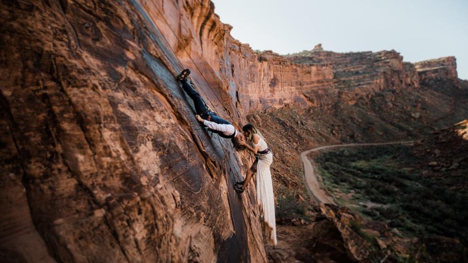 A bride and groom kiss upside down as they climb a mountain.