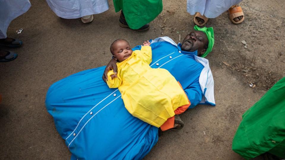 A man cradles a baby. Other people stand around in a circle.