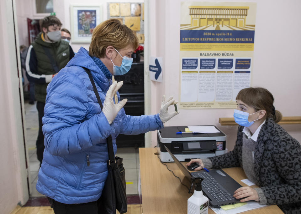 A woman, wearing face masks to protect against coronavirus shows an ID card as she arrives at a polling station during parliamentary elections in Vilnius, Lithuania, Sunday, Oct.11, 2020. Polls opened Sunday for the first round of national election in Lithuania, where voters will renew the 141-seat parliament and the ruling four-party coalition is widely expected to face a stiff challenge from the opposition to remain in office. (AP Photo/Mindaugas Kulbis)