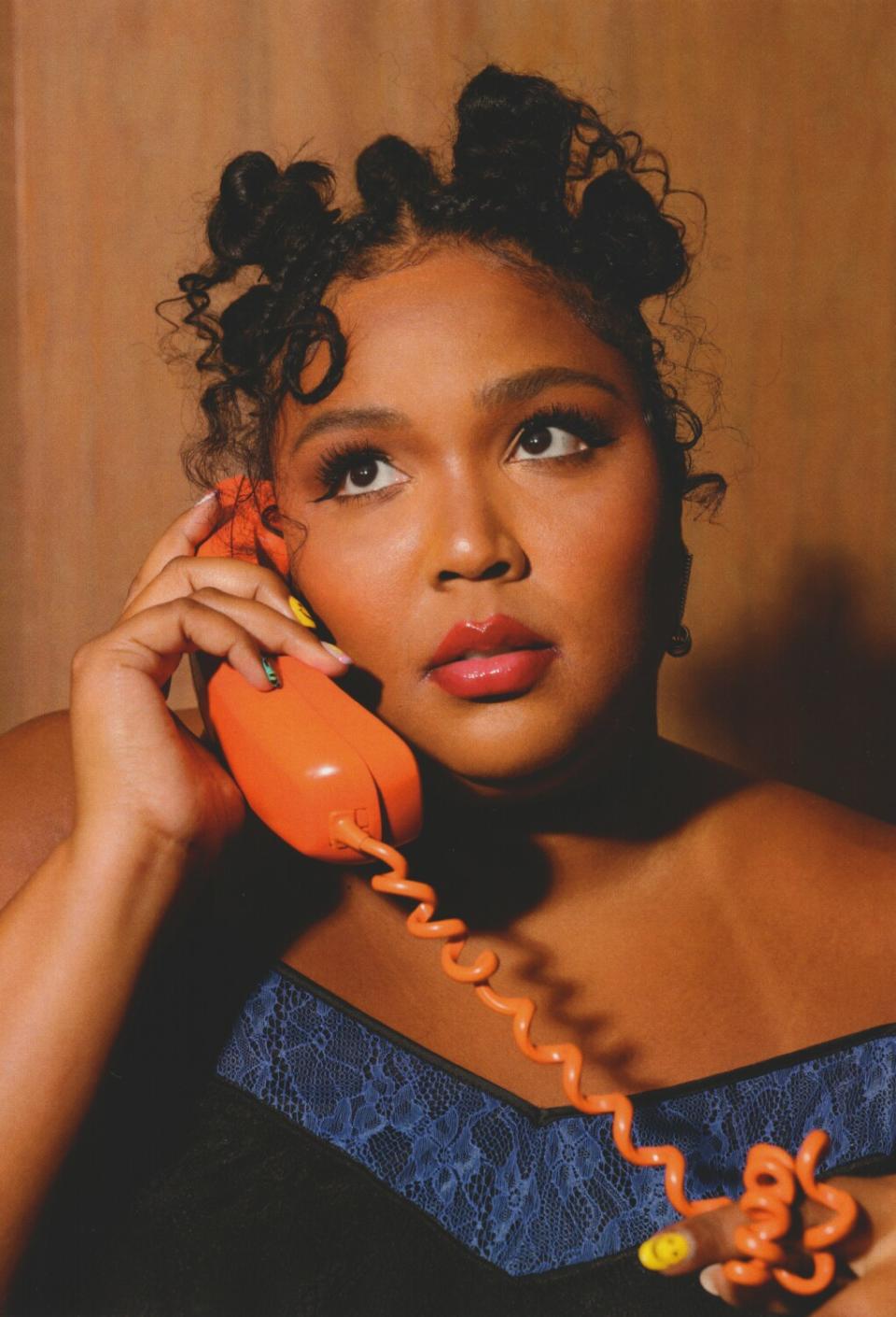 A woman holds an orange phone with an orange cord wrapped around her finger.