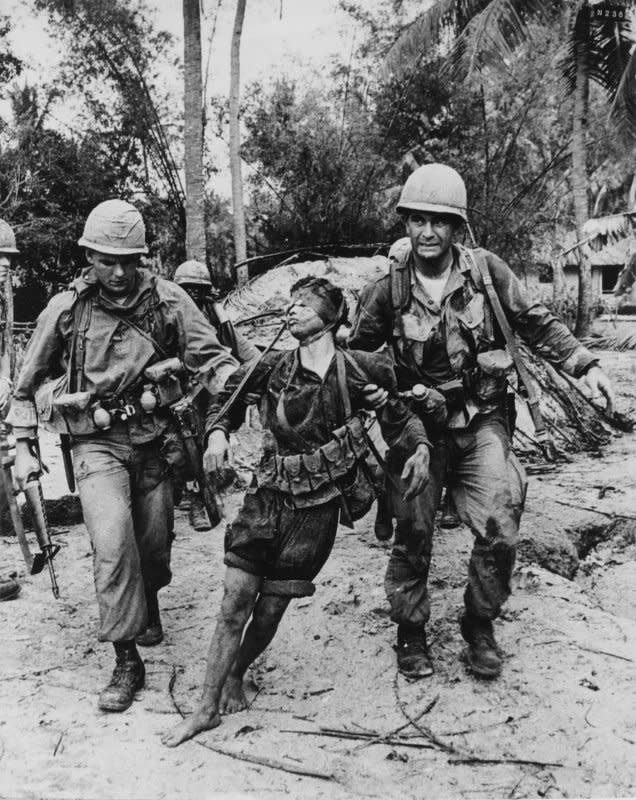 An injured North Vietnamese soldier is led from his bunker by soldiers of the U.S. First Cavalry Division. On July 28, 1965, President Lyndon B. Johnson announced he was dispatching 50,000 more U.S. troops to South Vietnam almost immediately, doubling monthly draft calls. File Photo by Kyoichi Sawada/UPI