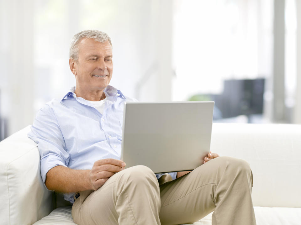 Older man sitting on couch holding laptop