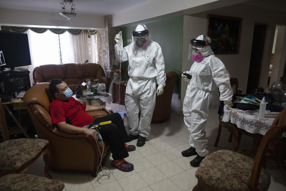 Angels of the Road volunteer paramedic Zully Rodiz, right, and Dr. Brayan Alfaro, measure the vital signs readings of a person suspected of having COVID-19, at his home in Caracas, Venezuela, Thursday, Feb. 11, 2021. The self-sufficient volunteer group, who seek their own funding and operate entirely independently of the government, are now prioritizing new coronavirus cases and offering free rides in their single ambulance to the hospital. (AP Photo/Ariana Cubillos)