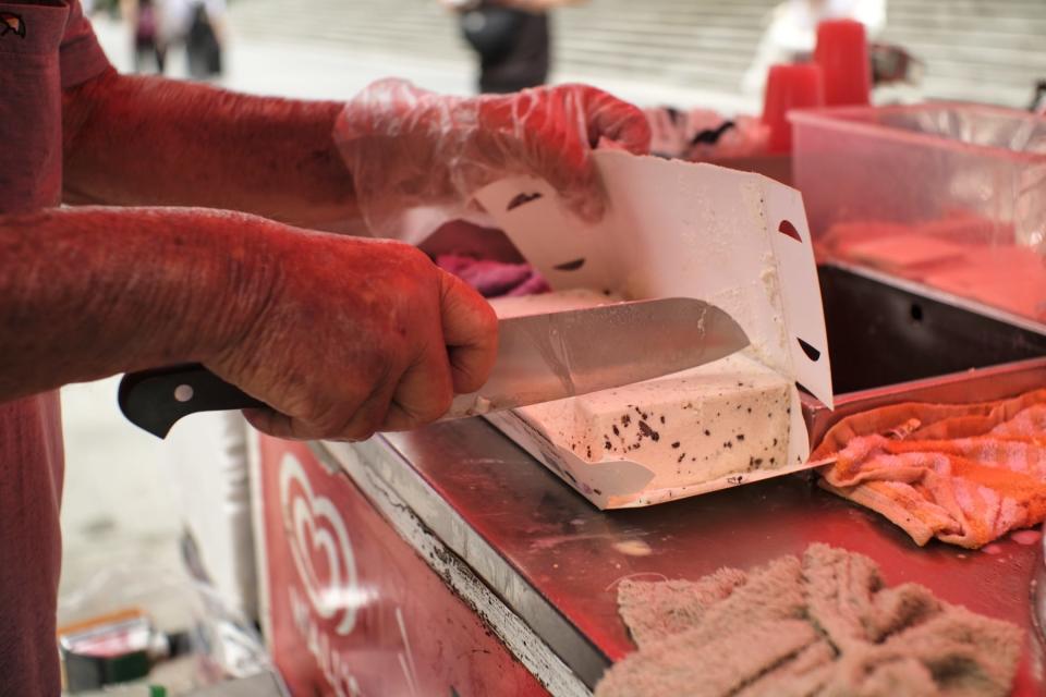 A close-up shot of an elderly man's wrinkled hands slicing ice cream into smaller blocks.