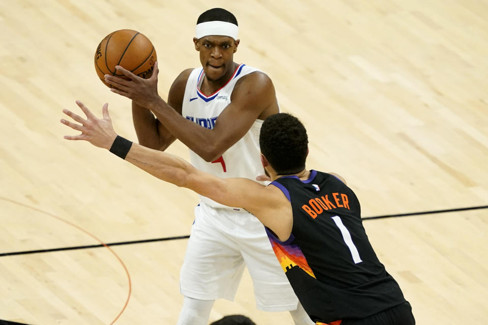 Rajon Rondo with the ball in his hands looking to pass around Devin Booker's outstretched hands. 