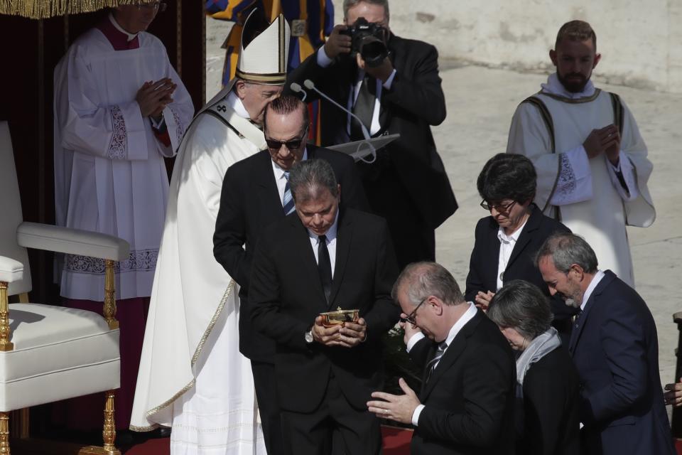 Jose Mauricio Moreira, center, of Salvador, whose healing from glaucoma was considered a miracle that led to the canonization of Dulce Lopes Pontes, leaves after meeting Pope Francis, background left, during a canonization Mass in St. Peter's Square at the Vatican, Sunday, Oct. 13, 2019. Francis presided over Mass on Sunday in a packed St. Peter's Square to declare Cardinal John Henry Newman and four women saints. (AP Photo/Alessandra Tarantino)