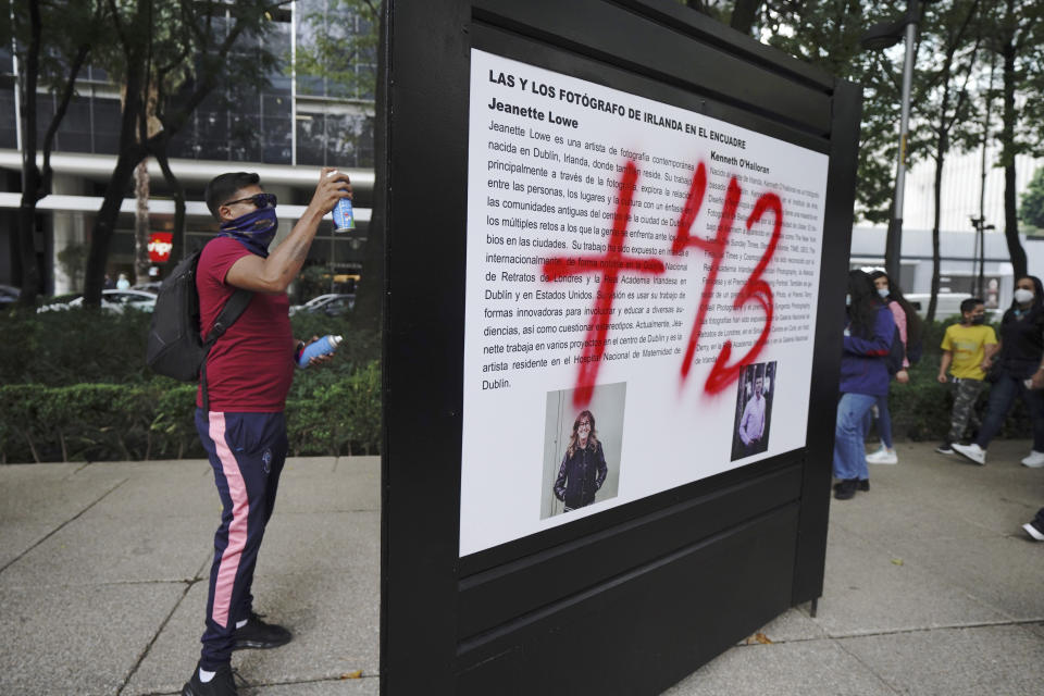 A demonstrator protesting the disappearance of 43 university students sprays graffiti on a display during a march on the seventh anniversary of their disappearance, in Mexico City, Sunday, Sept. 26, 2021. Relatives continue to demand justice for the Ayotzinapa students who were allegedly taken from the buses by the local police and handed over to a gang of drug traffickers. (AP Photo/Marco Ugarte)