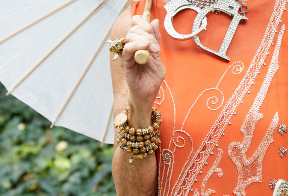 woman wearing an orange dress, two large silver statement necklaces, and stacked beaded bracelets while holding a parasol