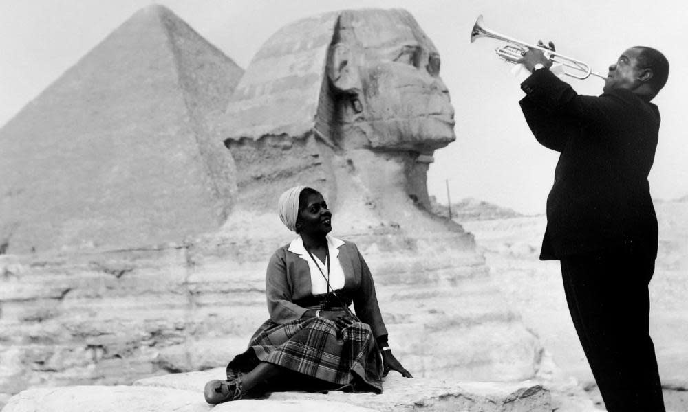 Louis Armstrong playing trumpet for his wife, Lucille, in front of the Great Sphinx and pyramids in Giza, Egypt.