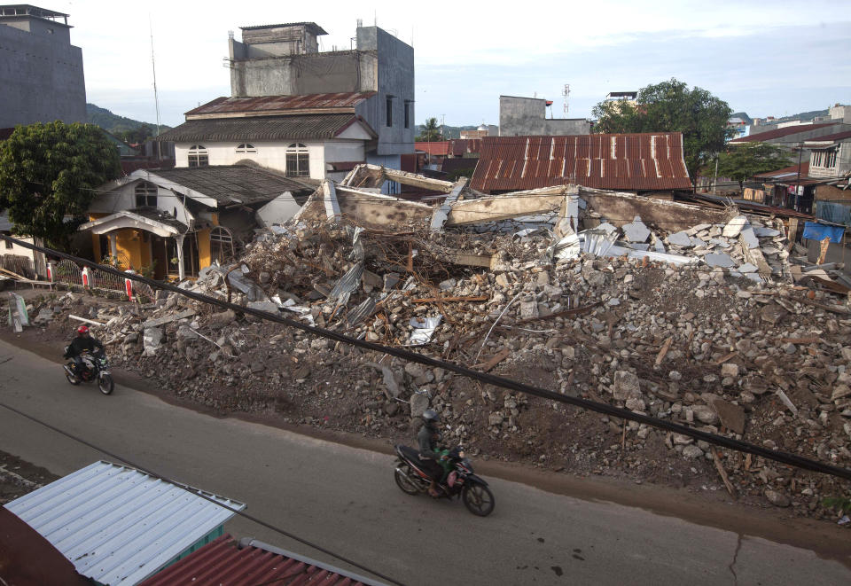 Motorists ride past buildings collapsed in Friday's earthquake in Mamuju, West Sulawesi, Indonesia, Monday, Jan. 18, 2021. Aid was reaching the thousands of people left homeless and struggling after an earthquake that killed a number of people in the province where rescuers intensified their work Monday to find those buried in the rubble. (AP Photo/Yusuf Wahil)