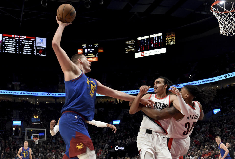 Denver Nuggets center Nikola Jokic, left, holds off Portland Trail Blazers guard Delano Banton, center, and forward Jabari Walker, right, during the first half of an NBA basketball game in Portland, Ore., Friday, Feb. 23, 2024. (AP Photo/Steve Dykes)