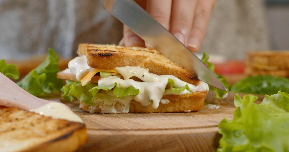A chef cutting a sandwich full of mayonnaise and other condiments in half. (Photo via Getty Images)