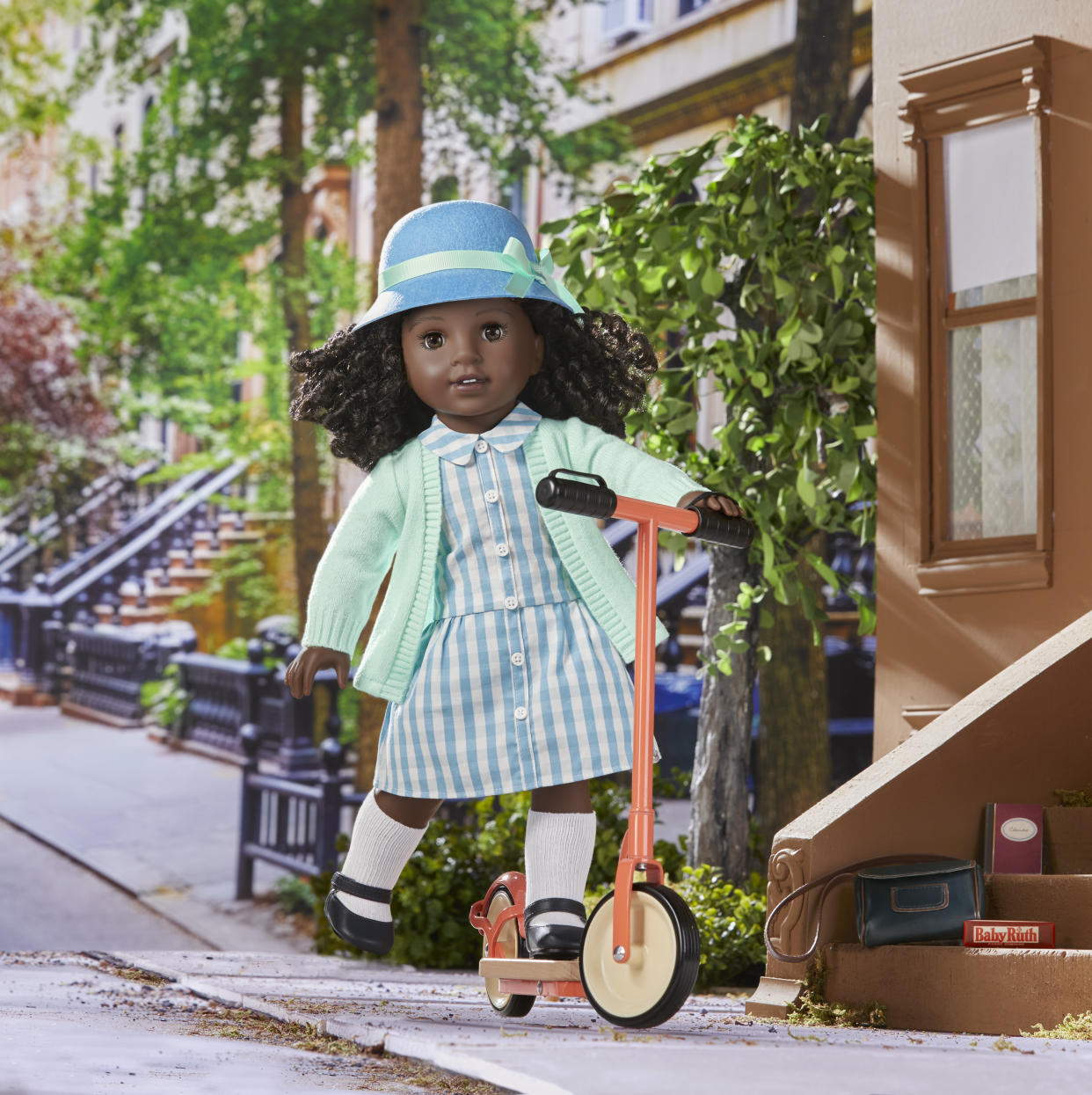 Claudie comes dressed in a woven blue-and-white plaid dress and knit cardigan with black Mary Janes, a heart-shaped necklace and a cloche hat. (Photo: American Girl)