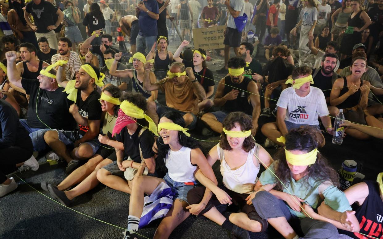 Protesters, wearing a yellow blindfold, sit on the ground during an anti-government rally