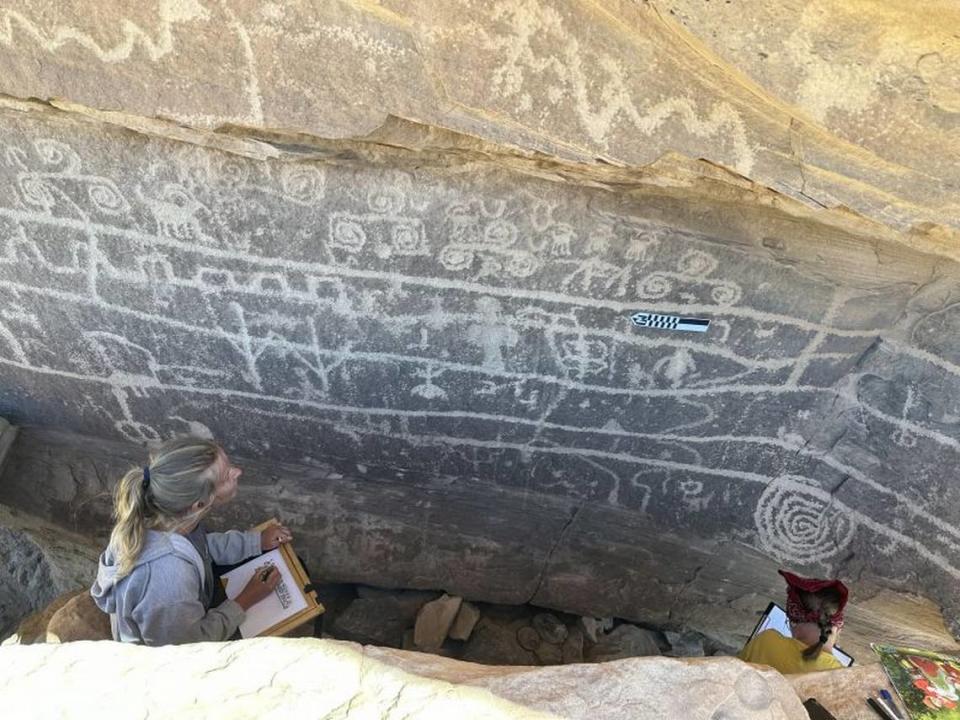 Archaeologists surveying a wall of carvings.