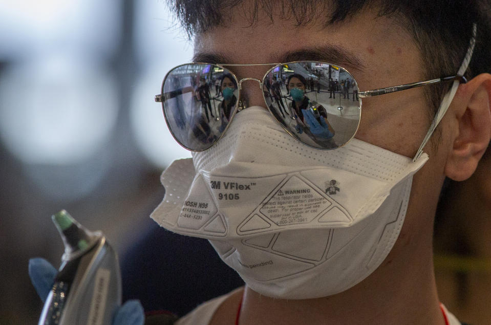 A health worker with a thermometer is mirrored in a sun glasses of a tourist from Wuhan, China as he stands in a line for a charter flight back to Wuhan at the Suvarnabhumi airport, Bangkok, Thailand, Friday, Jan. 31, 2020. A group of Chinese tourists who have been trapped in Thailand since Wuhan was locked down due to an outbreak of new virus returned to China on Friday. (AP Photo/Gemunu Amarasinghe)