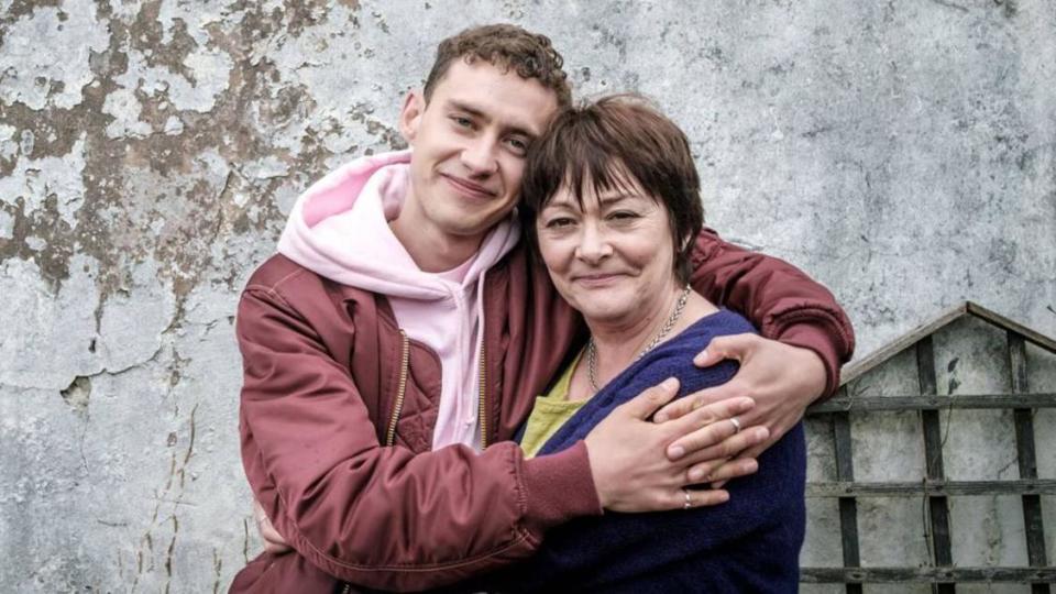 Olly Alexander hugging his mum standing in front of a grey wall