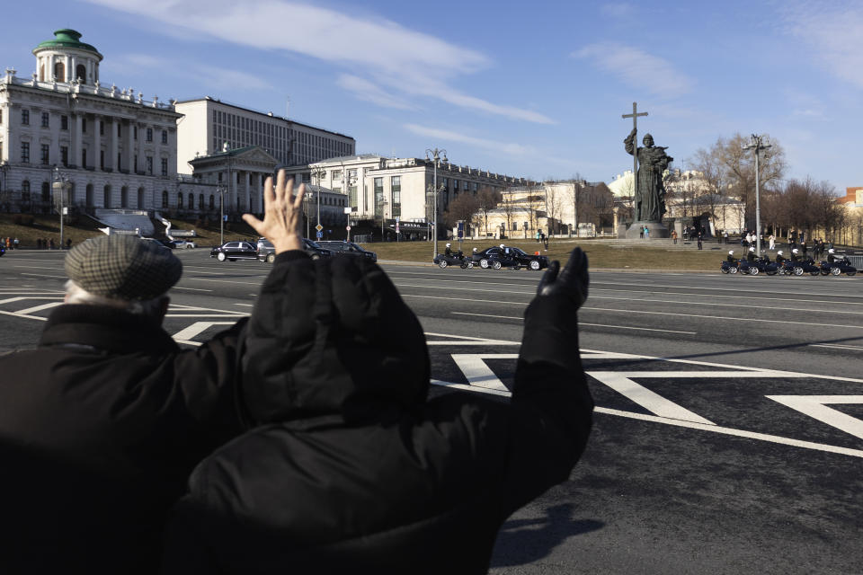 People wave Chinese President Xi Jinping's motorcade driving toward The Kremlin with the statue of Vladimir the Great in the background in Moscow, Russia, Tuesday, March 21, 2023. (AP Photo)
