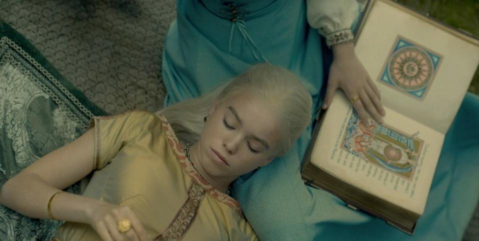 Rhaenyra lies in Alicent's lap next to an illustrated book