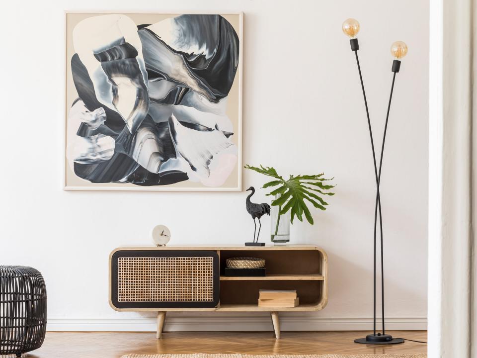 A room with white walls with a low console table, two-bulb lamp, and statement, black-and-white piece of art on the wall