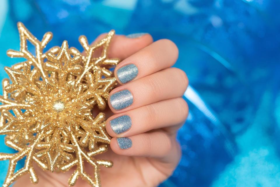 female hand with blue nail design glitter blue nail polish manicure model hand hold gold christmas star decoration on blue background holiday manicure concept