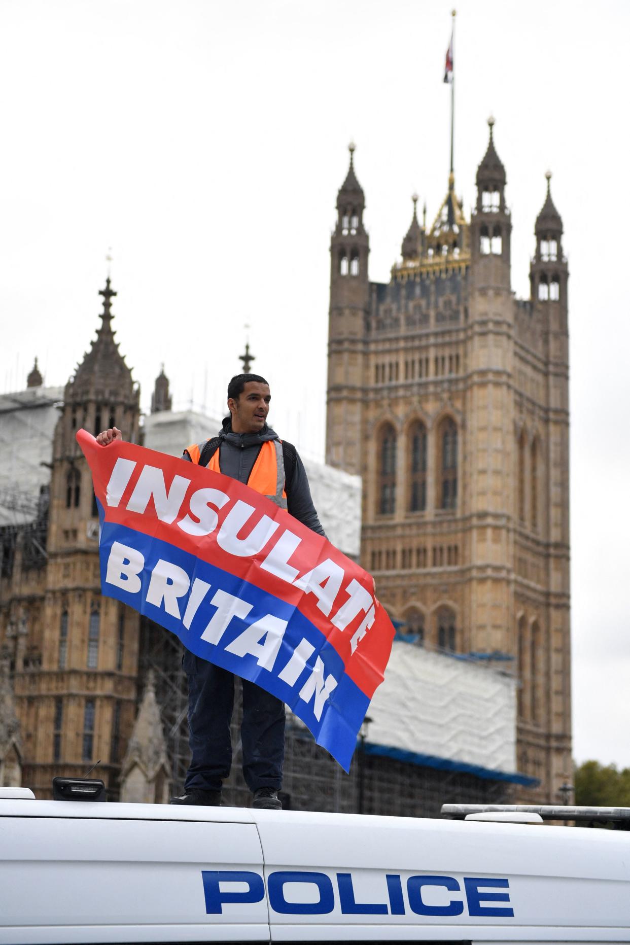 An environmental activist from the group Insulate Britain waves a banner from atop a police van at Parliament Square in central London on November 4, 2021, as protestors call for the UK government to fund the insulation of Britain's homes. - Insulate Britain, a new group whose campaigners have repeatedly blocked roads and motorways in and around the capital, want the government to insulate all British homes starting with social housing. (Photo by JUSTIN TALLIS / AFP) (Photo by JUSTIN TALLIS/AFP via Getty Images)