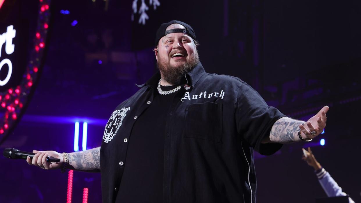 jelly roll holding out his arms and smiling while performing during a concert