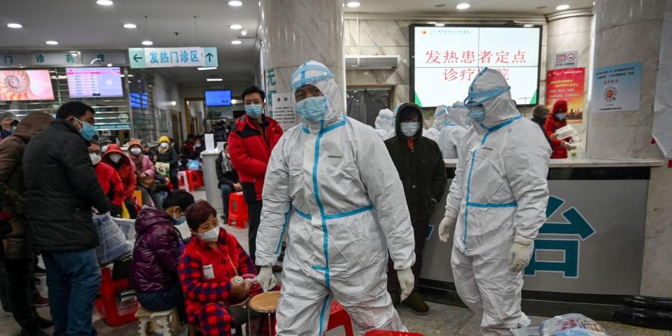 Medical staff members wearing protective clothing to help stop the spread of a deadly virus which began in the city, walk next to patients (L) waiting for medical attention at the Wuhan Red Cross Hospital in Wuhan on January 25, 2020.