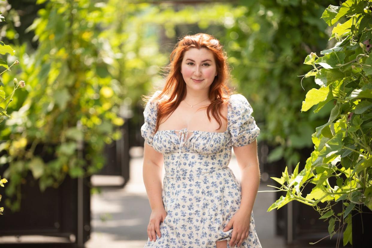 OnlyFans creator Isla Moon in a white dress with blue flowers, standing amid plants in a garden.