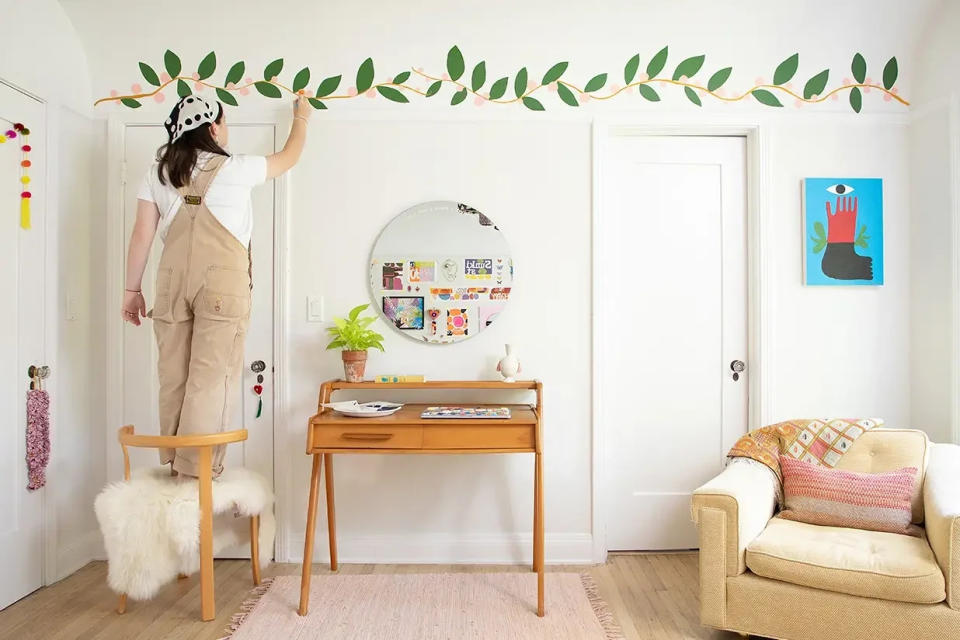 Teen painting her bedroom with a green vine along top wall. 