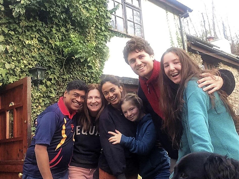 In this image taken in Oct. 2019 Dr. Poorna Gunasekera, left, poses for a photo with his family from second left: his partner Hayley Newman, daughter Saki, Natty (Hayley's daughter), Saki's boyfriend George Petrie, Mia (Hayley's oldest daughter) and Barney the dog. At his darkest moment in his struggle with the coronavirus, Dr. Poorna Gunasekera glimpsed the first rays of light when three of his former students came to help. Having endured a severe deterioration in his COVID-19 symptoms after around 12 days of contracting the virus, Gunasekera was rushed to Derriford Hospital in Plymouth, in the early hours of March 30. "It was wonderful that during that time, two of my former students, who are doctors, and another who was a nurse, actually came and they identified themselves," he told The Associated Press over several interviews following his release from hospital on April 9. (George Petrie via AP)