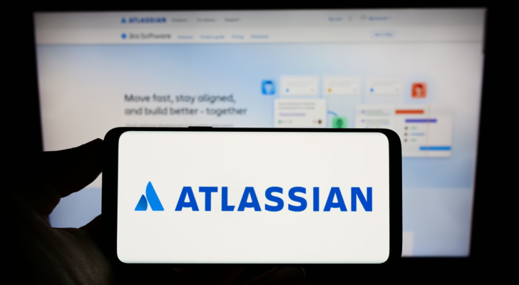 Person holding cellphone with logo of Australian software company Atlassian Corporation (TEAM) on screen in front of webpage. Focus on phone display. Unmodified photo.