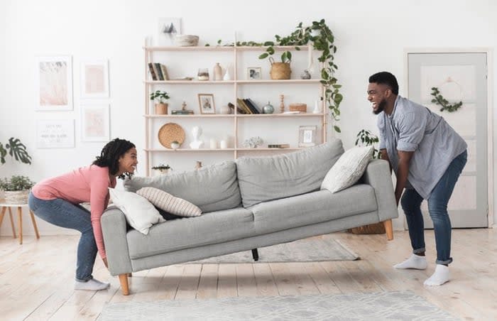 A smiling man and woman moving a couch into the living room in their new home.