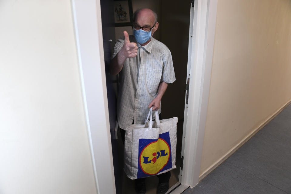 Peter Kraus gestures after receiving a food delivery from the Rev. April Keech an Anglican priest, in London, Saturday, March 28, 2020. Keech and her team of volunteers have spent the past two weeks buying groceries, filling prescriptions and making deliveries to residents in east London who are at risk of serious illness or death from the COVID-19 disease. The new coronavirus causes mild or moderate symptoms for most people, but for some, especially older adults and people with existing health problems, it can cause more severe illness or death. (AP Photo/Alberto Pezzali)