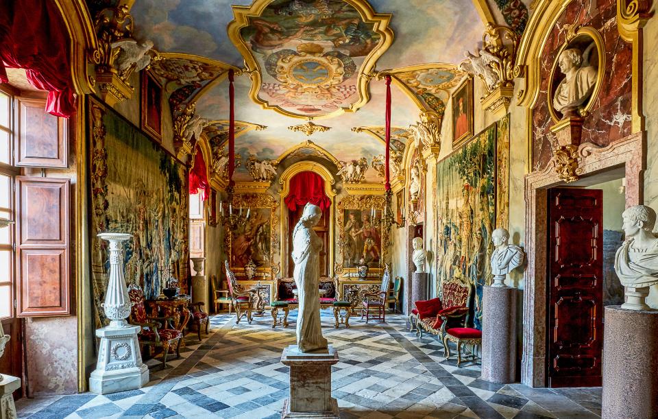 A marble sculpture of Athena stands at the center of the imperial roman–style grand gallery. 17th-century busts and Sicilian floor tiles; curtains of a Veraseta silk faille.