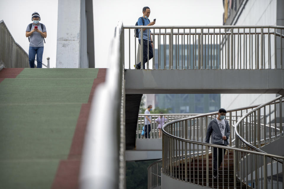 People wearing face masks to protect against COVID-19 walk across a pedestrian bridge during the morning rush hour in Beijing, Wednesday, Aug. 4, 2021. China's worst coronavirus outbreak since the start of the pandemic a year and a half ago escalated Wednesday with dozens more cases around the country, the sealing-off of one city and the punishment of its local leaders. (AP Photo/Mark Schiefelbein)