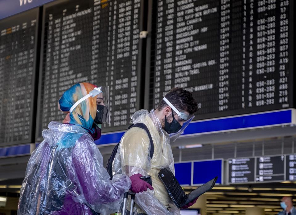 Passengers with protection gear walk past the flight board at the airport in Frankfurt, Germany, Friday, July 24, 2020. (AP Photo/Michael Probst)