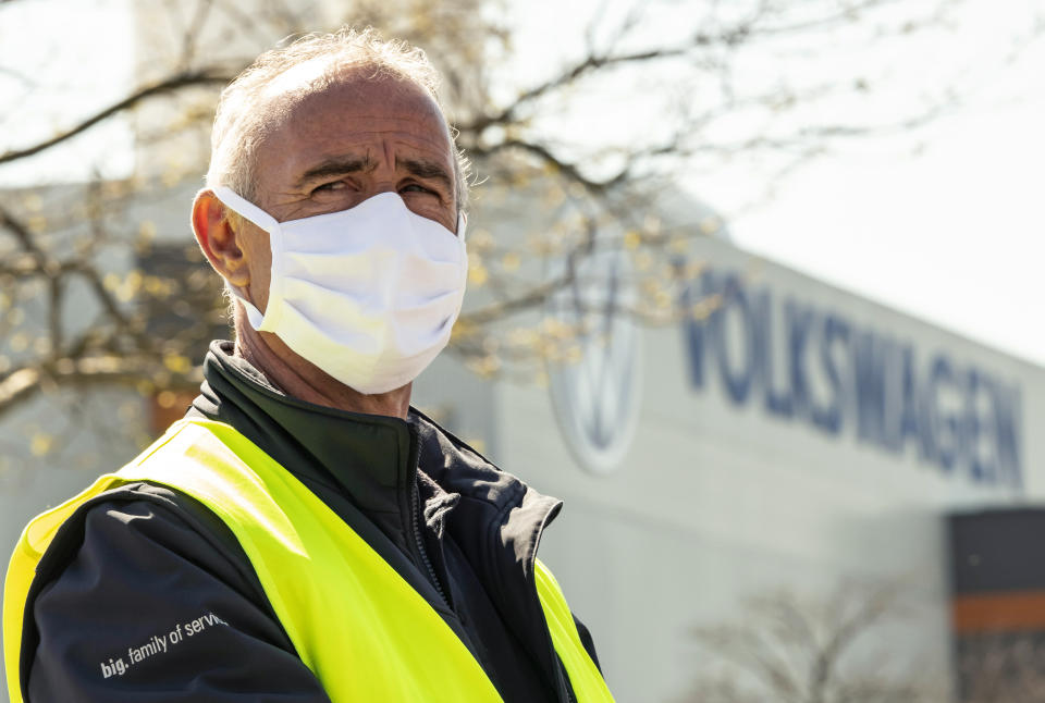 An employee wearing a face mask in front of a factory building during the production restart of the plant of the German manufacturer Volkswagen AG (VW) in Zwickau, Germany, Thursday, April 23, 2020. Volkswagen starts with step-by-step resumption of production. The car company are completely converting the plant in Zwickau from 100 percent combustion engine to 100 percent electric. (AP Photo/Jens Meyer)