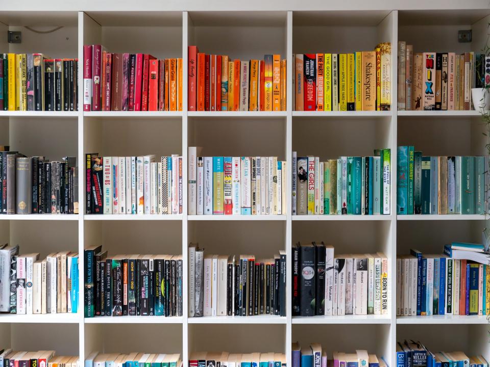 White book shelf filled with books that are organized by color