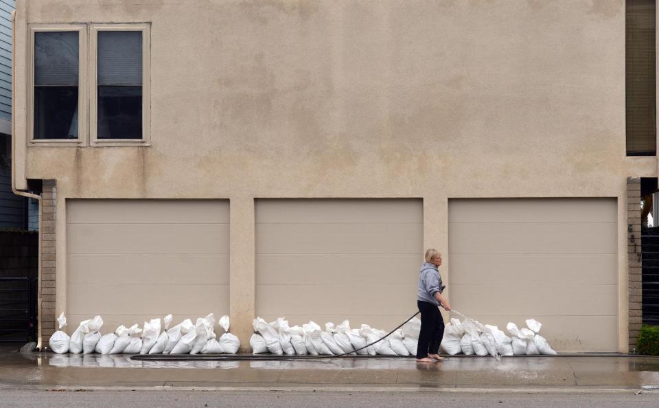 A resident hoses off a neighbor's driveway along Ocean Boulevard between 66th and 72nd Place, in Long Beach, Calif., Sunday, March 2, 2014. Flooding occurred when heavy surf eroded the protective sand berm Saturday night, resulting in 20 homes on Ocean Blvd between 66th and 72nd Place, sustaining damage to either living levels or parking areas. No residents were reported to be displaced, said Long Beach Fire Department Public information Officer Will Nash. (AP Photo/Daily Breeze, Stephen Carr)